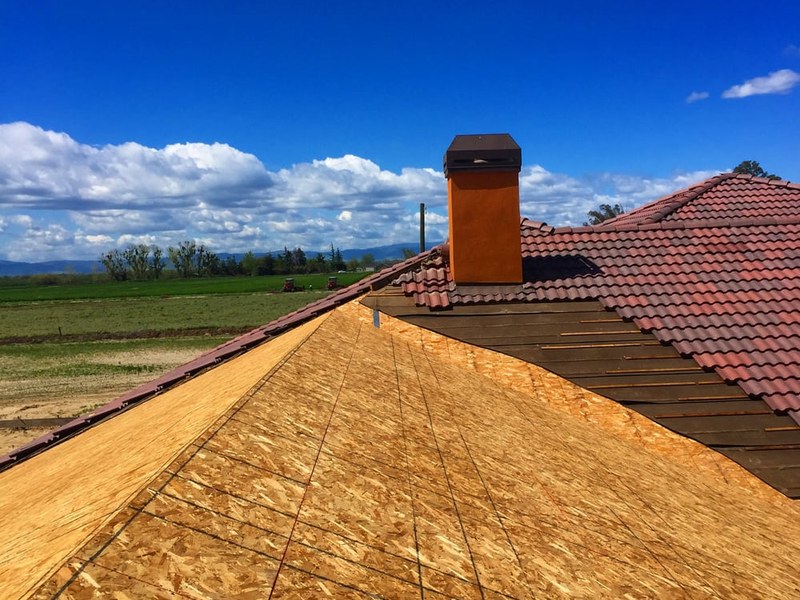 DeHart Roofing crew mid-install on a rural Stanislaus County tile roof — new OSB decking down, original tile retained